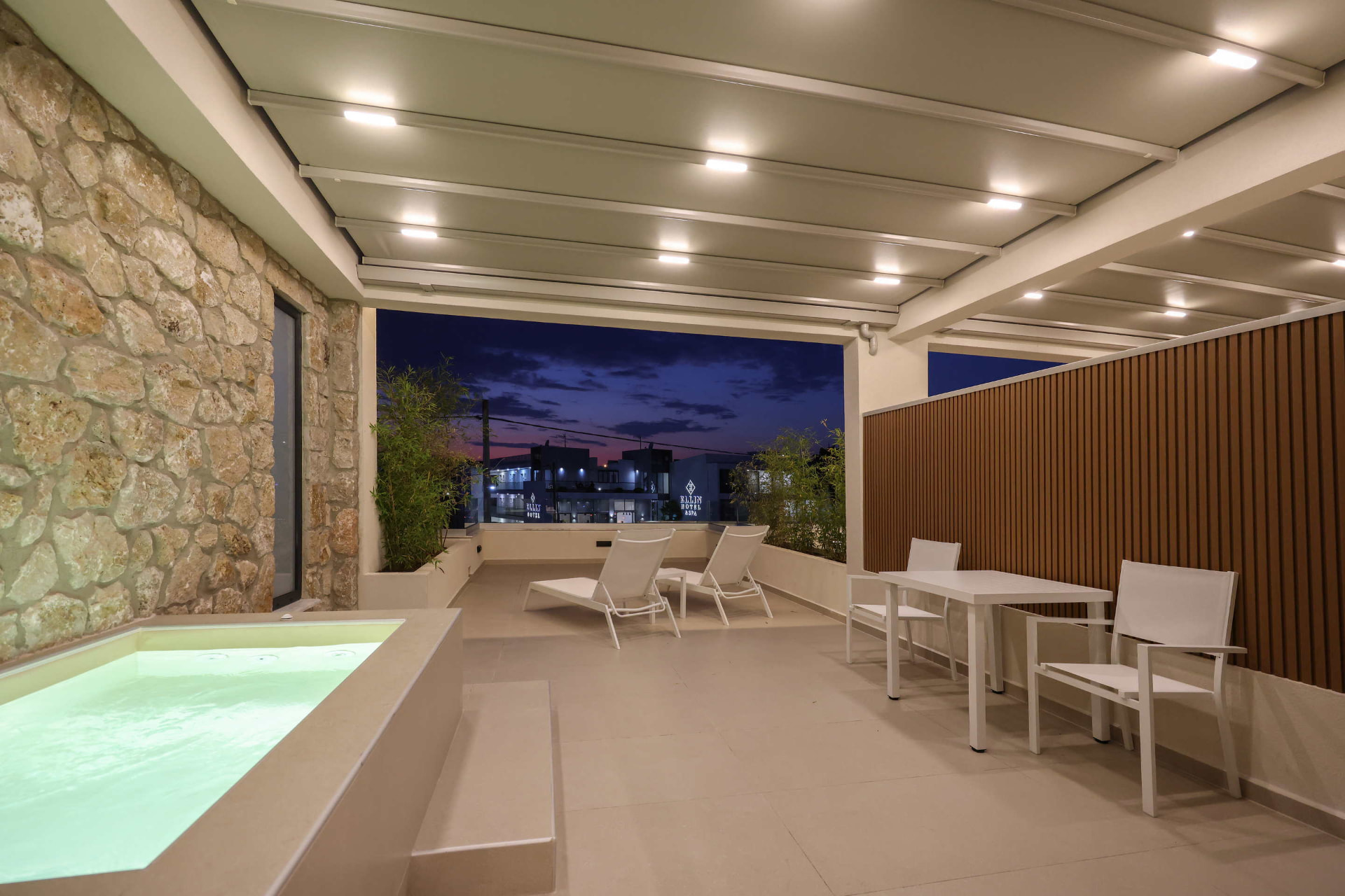 Private terrace with glowing Jacuzzi, dining table and evening sky beyond